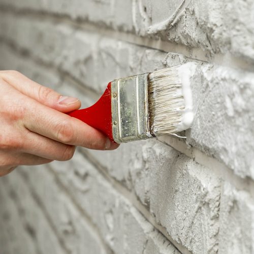 Male's hand painted with brush white brick wall. Renovation work. White background.